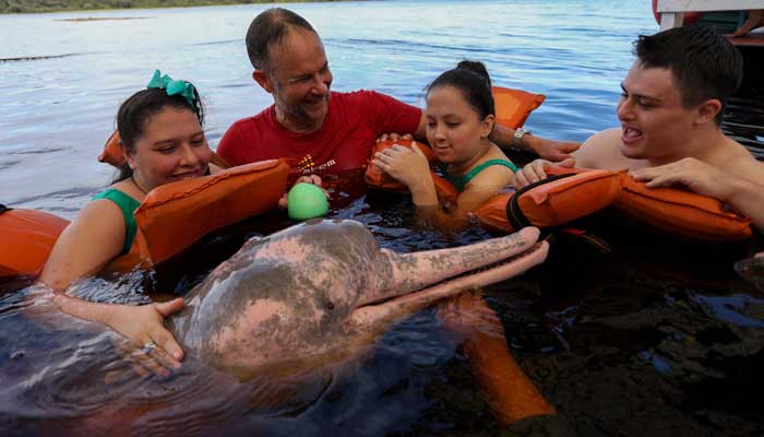 Physical therapist Igor Simoes Andrade and Young People with Disability Swim with Pink Dolphins (Inia Geoffrensis) on the Rio Negro River in Iranduba, Amazon State, Brazil, February 20, 2025. - AFP
