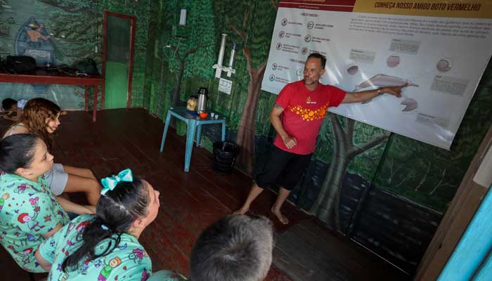 Physical therapist Igor -simos Andrade teaches pink dolphins (Inia geoffensis) to young people with disabilities before swimming with them on a floating boat on the Rio Negro River in Iranduba. - AFP