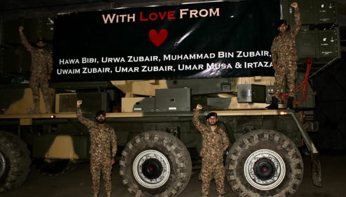 This undated image shows Pakistani army soldiers posing with an armed vehicle decorated with a banner with the names of the children martyred by India's cowardly missile strikes recently. - Ispr