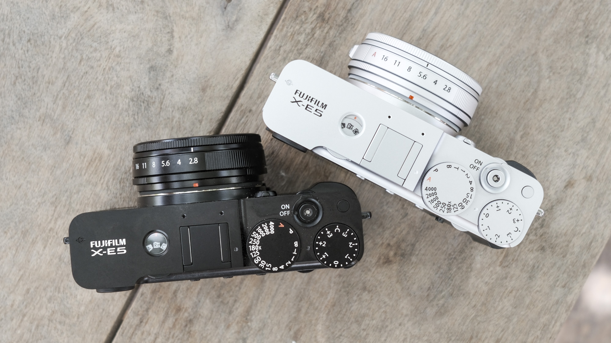 Top down all black Fujifilm X-E5 along with Silver Fujifilm X-E5, on a wooden bench