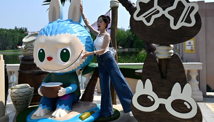 A woman puts to a picture next to the character Labubu as she visits Pop Mart Theme Park Pop Land in Beijing, China on June 18, 2025. - AFP