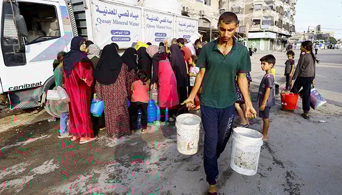 A man wearing buckets of water while Palestinians are waiting to collect water in the middle of deficiency, in Gaza City 6 August 2025. - Reuters