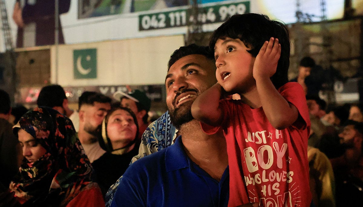 A child covers his ears when he sees fireworks with his father during Independence Day Celebration in Lahore on August 14, 2025. - Reuters