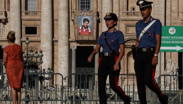 Carabinieri passes a picture hanging from the facade of St Peter's Basilica by the Vatican, depicting a picture of Carlo Acutis, a British-born Italian boy who becomes the first millennium made into a Catholic saint in a ceremony led by Pope Leo, as seen from Rome, Italy,