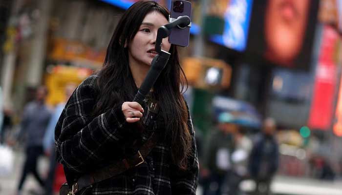 A woman makes a video with a cell phone to send on Tiktok as she stands at Times Square in New York City, New York, USA, March 13, 2024. - Reuters