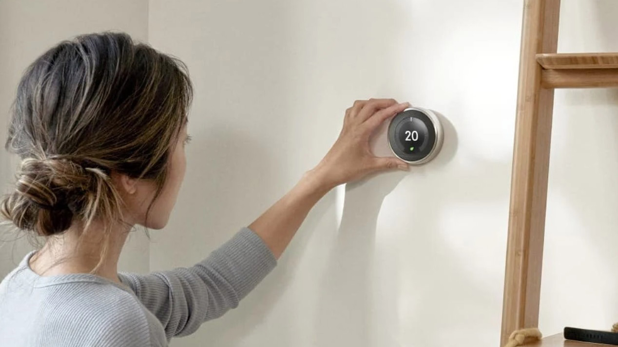 Nesten's learning thermostat mounted on a wall controlled by a woman