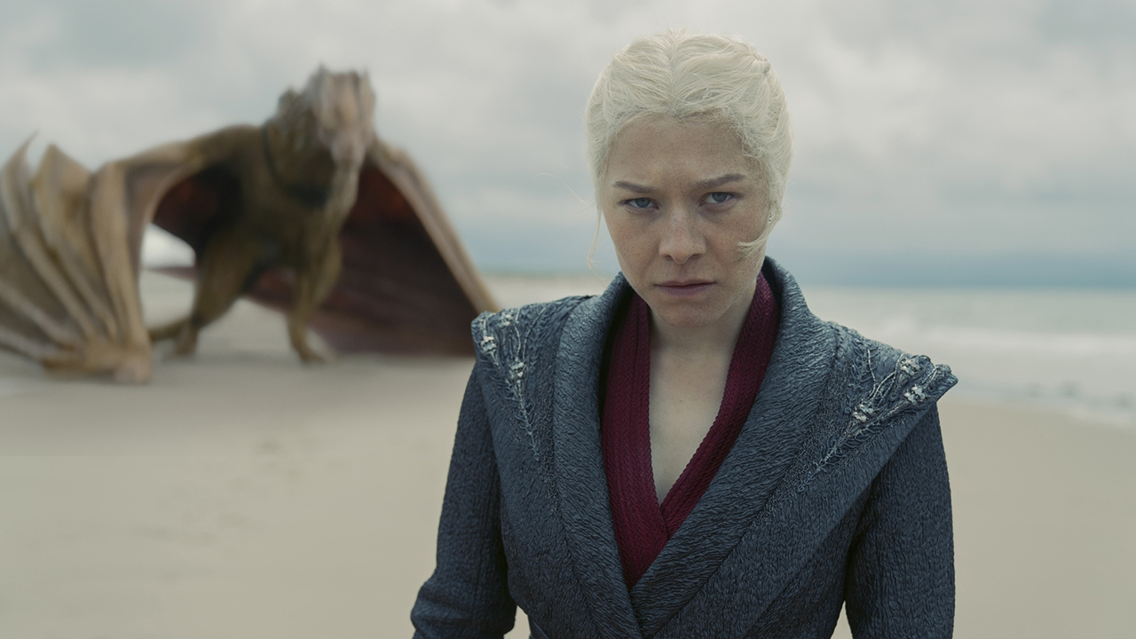 Rhaenyra Targaryen scowls as she stands on a beach with Syrax in the background in House of the Dragon Season 2