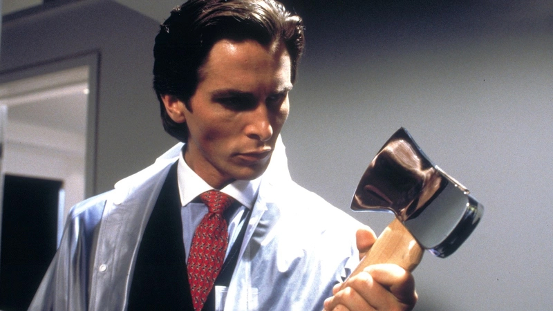 A still from the movie American Psycho, where Patrick Bateman (Christian Bale) wears a suit and looks at an EACS.