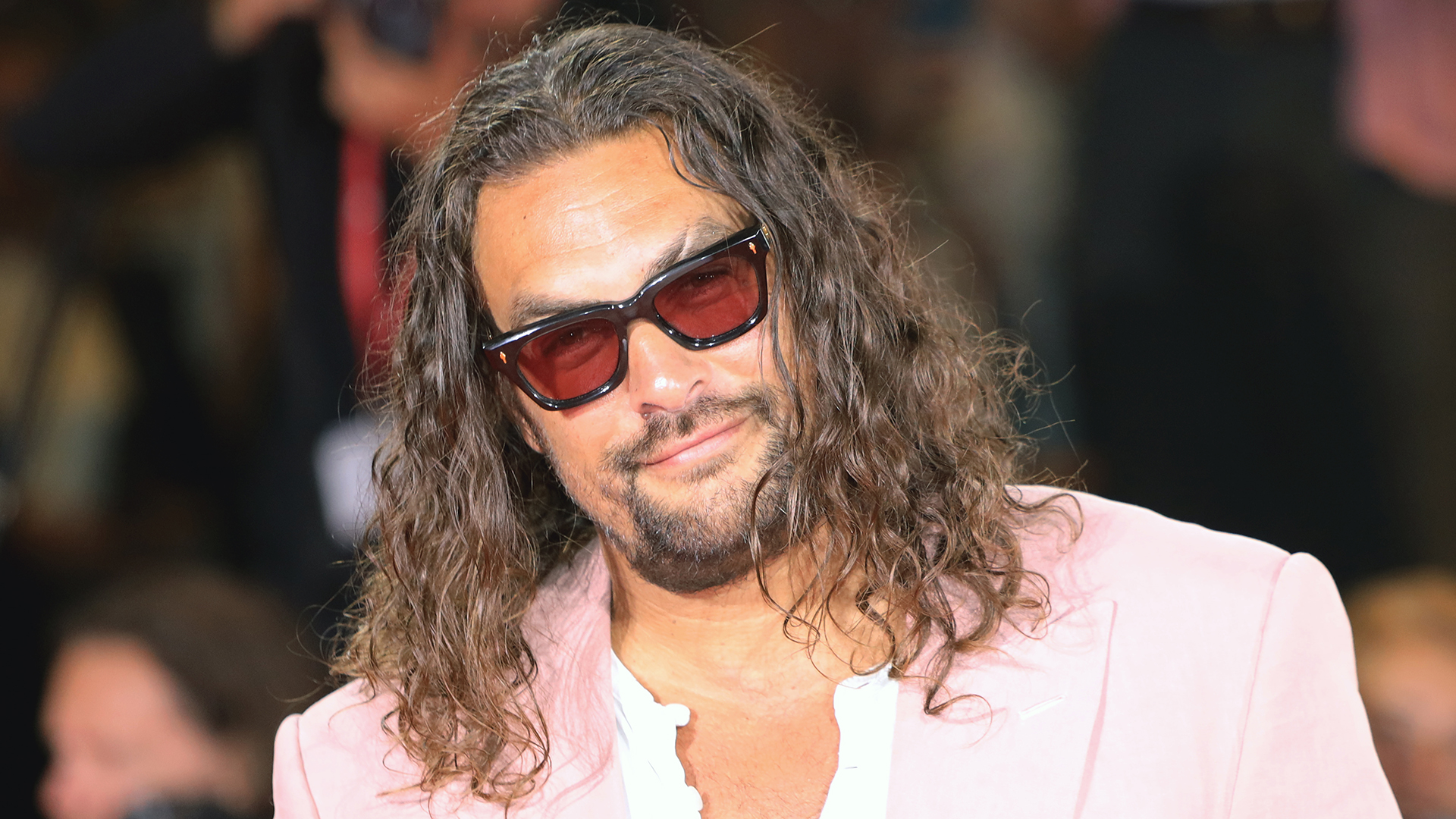 Jason Momoa wearing sunglasses and posing for photographs on a red carpet