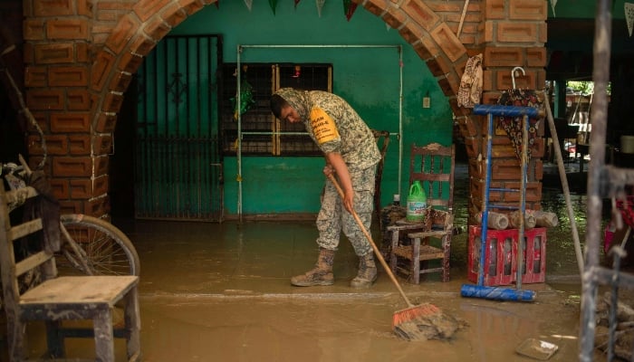 A Mexican army soldier works to remove the mud from a flooded house due to the heavy rain in the municipality of Alamo, Veracruz, Mexico, on October 12, 2025. - AFP