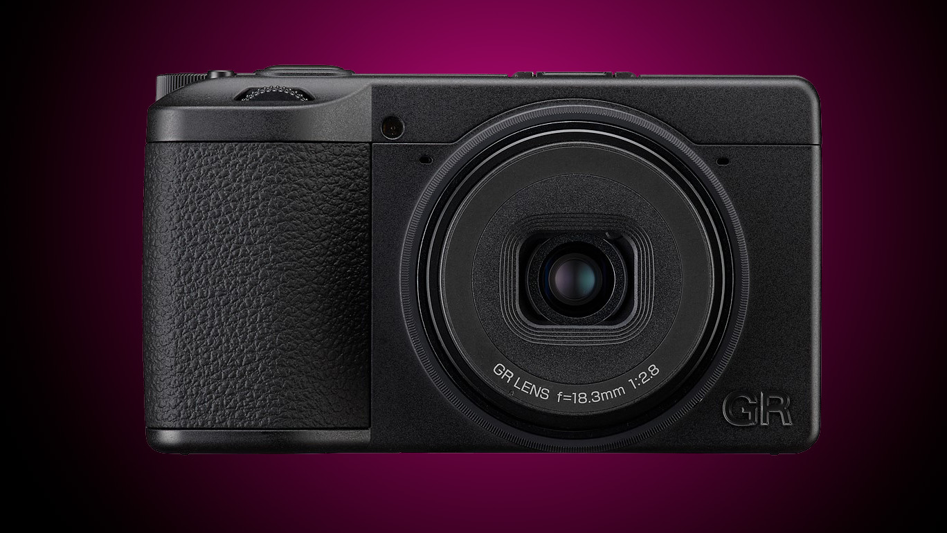 A Ricoh compact camera against a graduated purple background