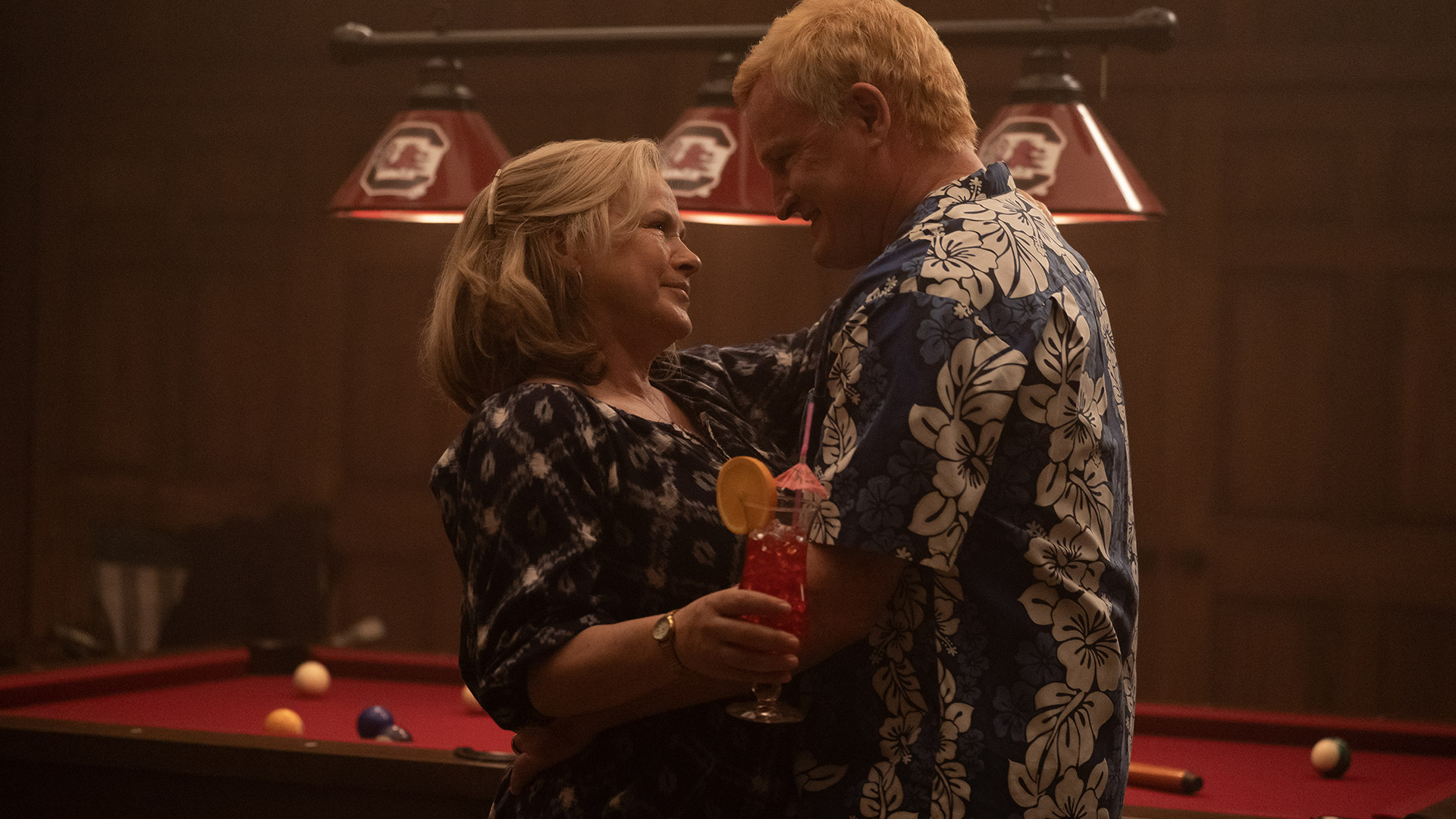 Patricia Arquette and Jason Clarke embrace while standing in front of a pool table in Murdaugh: Death in the Family