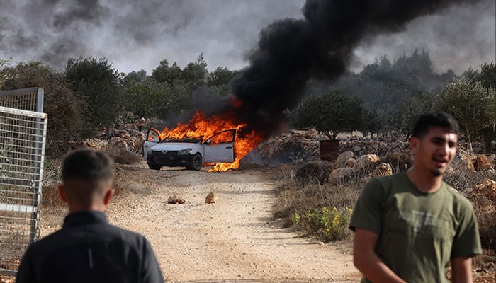 Palestinians stand near a burning car allegedly set on fire by Israeli settlers who tried to disrupt them harvesting olives near the occupied West Bank village of Turmos Ayya near Ramallah on October 19, 2025. — AFP