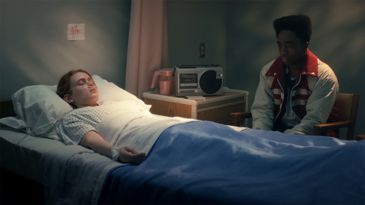 Max a comatose, lying in a hospital bed as Lucas sits next to her in Stranger Things season 5