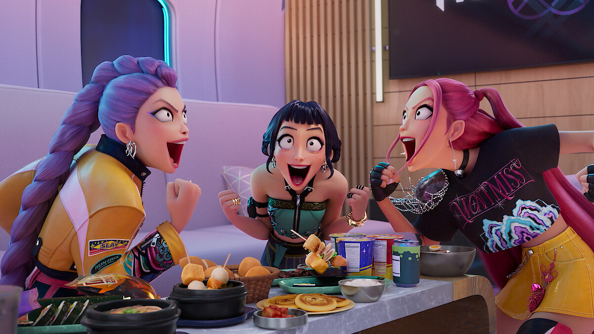 Rumi, Zoey and Mira cheer while sitting at a table full of food in Kpop Demon Hunters