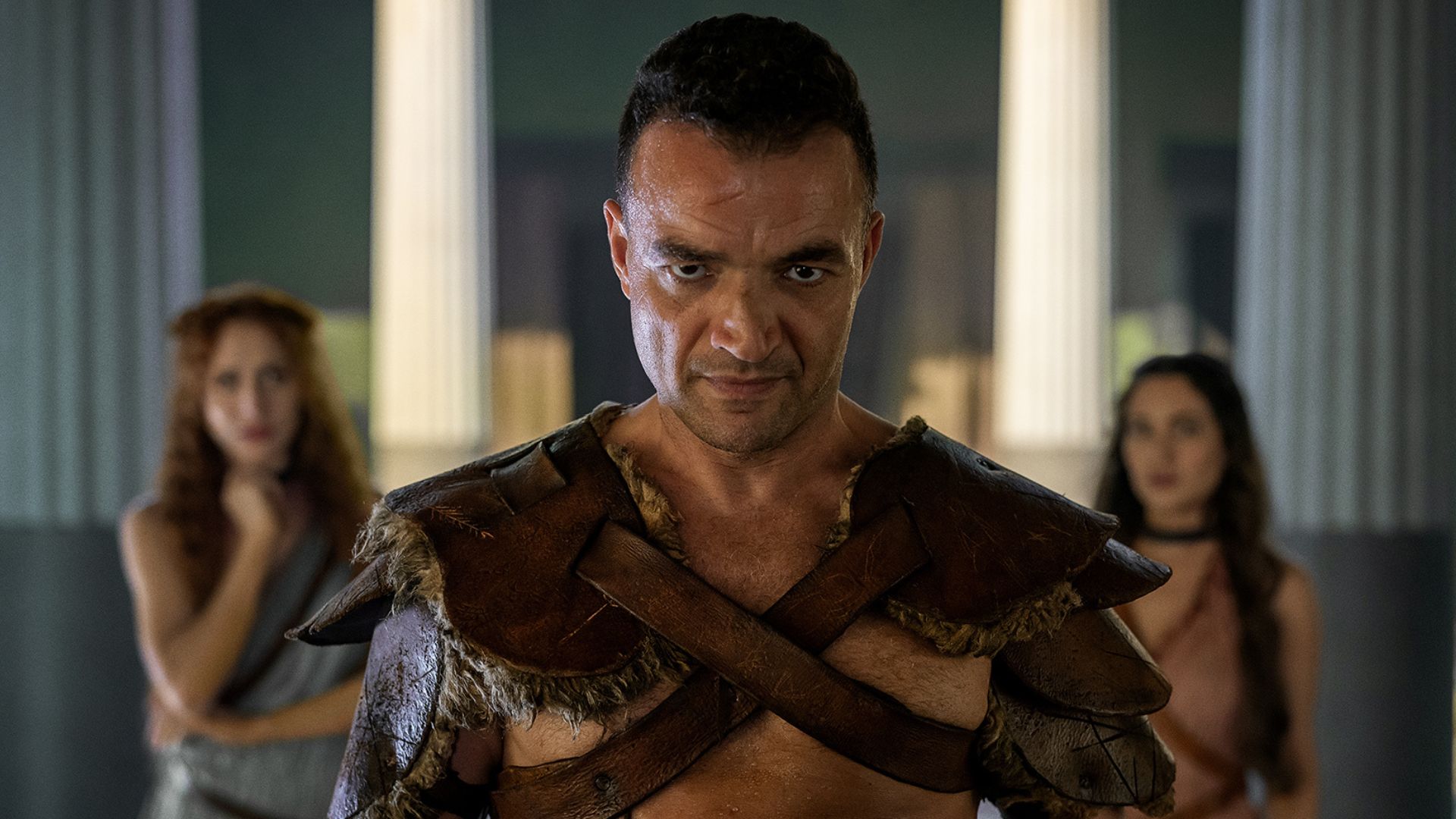 Ashur stands between two women who are in the background