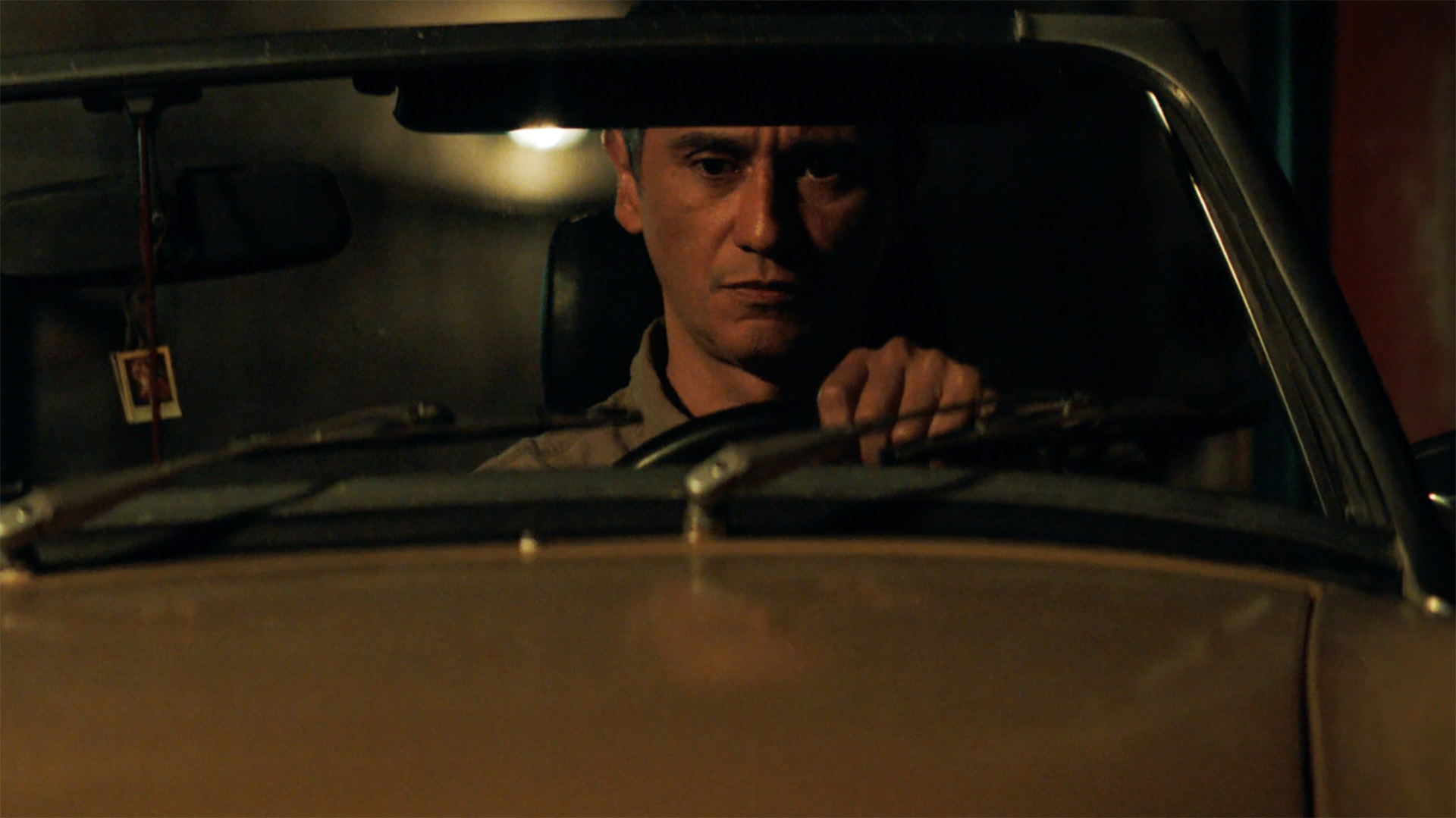 Manousos sits in his top-down car at night in Pluribus episode 5
