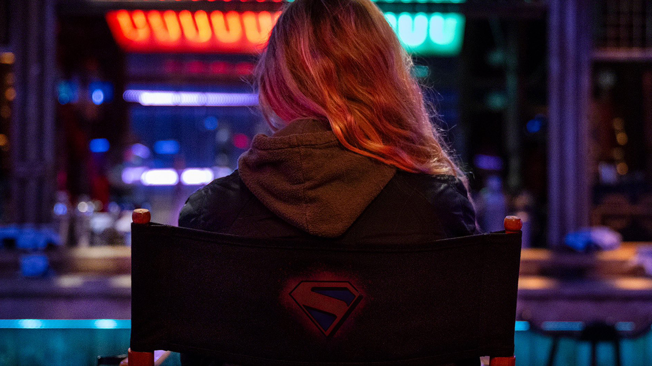A photo of Milly Alcock sitting on a chair with her back to the camera on the set of Supergirl: Woman of Tomorrow