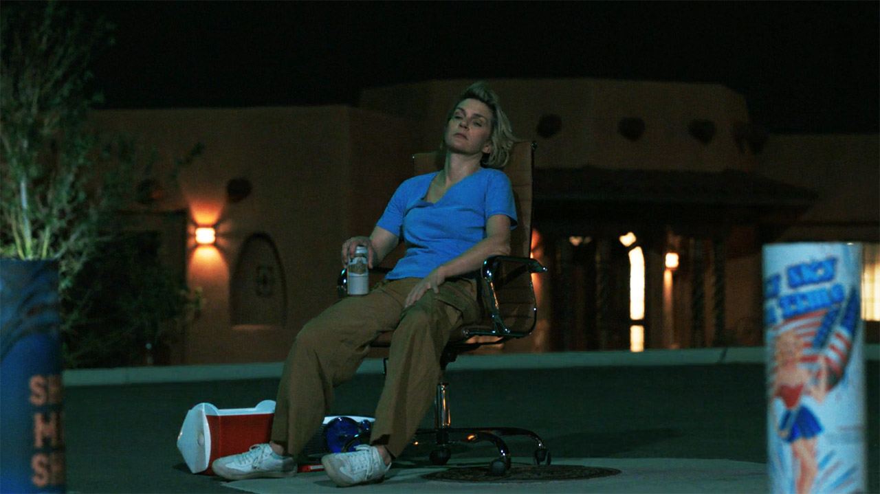 A seated Carol watches some fireworks at night in Pluribus episode 7