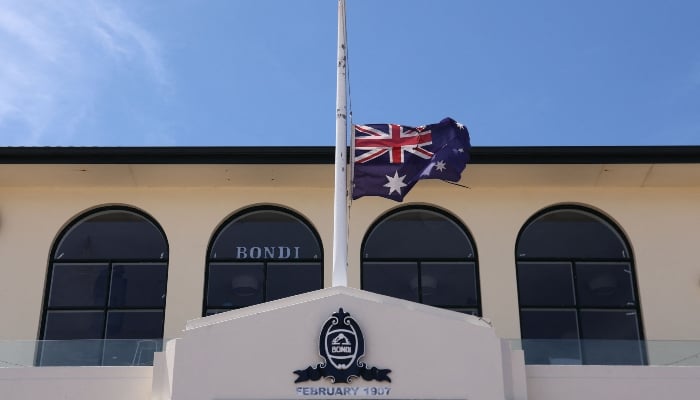 Australia's flag flies at half-mast at the Bondi Surf Bathers Life Saving Club near the boardwalk at Bondi Beach, where mourners have left floral tributes in honor of the victims of the Dec. 14 shooting there in Sydney, Dec. 18, 2025. — AFP
