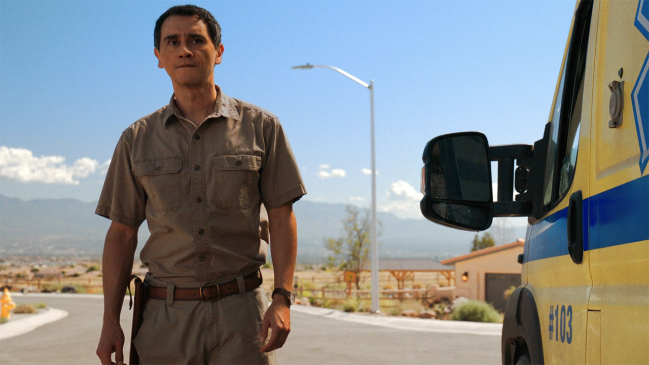 Manousos stands next to an ambulance in Pluribus episode 9