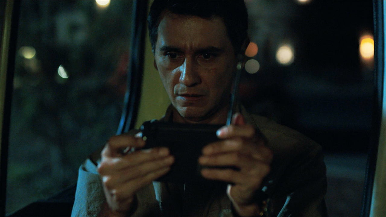 Manousos looks at a portable radio at night in Pluribus episode 9