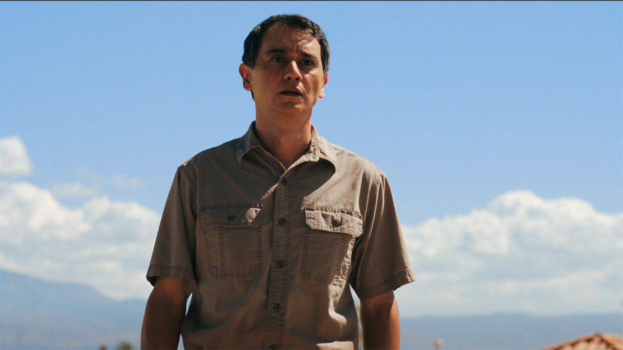 Manousos stands in front of Carol's home in Pluribus episode 9