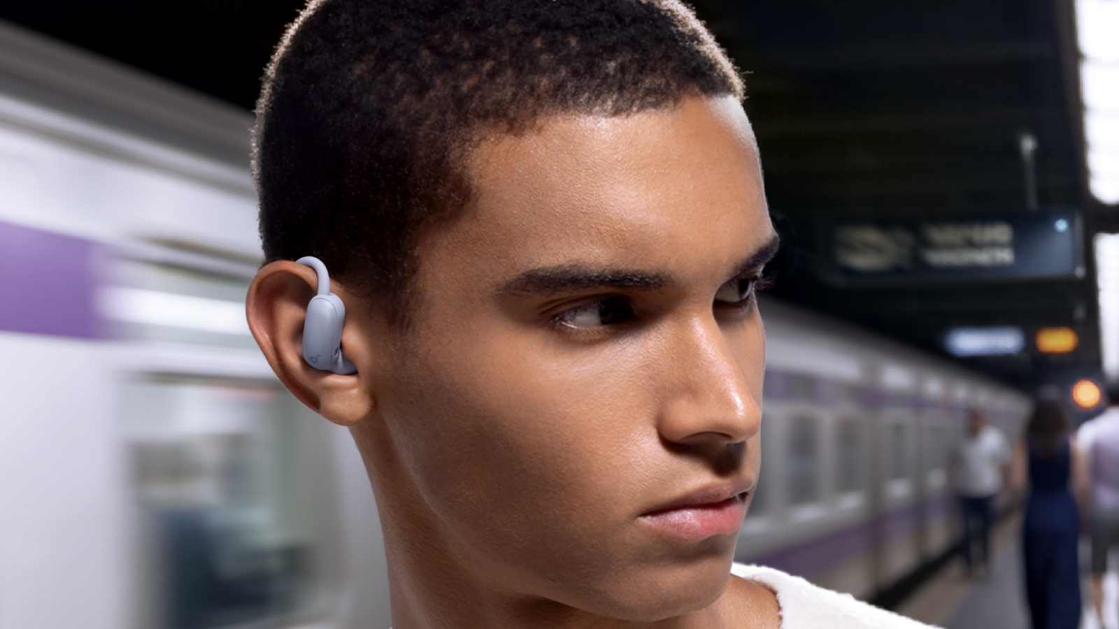 Anchor Soundcore Aerofit 2 Pro in a man's ear as he looks the wrong way to wait for the train.