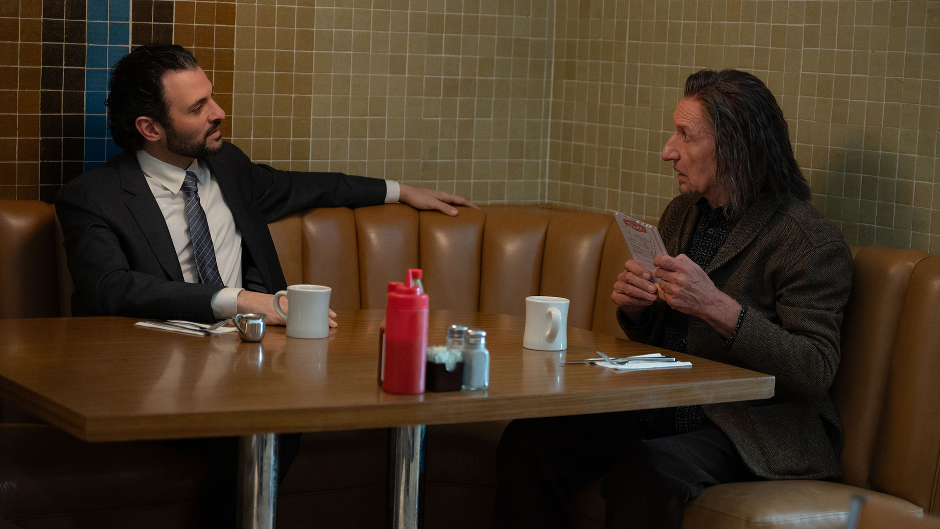DoDC Agent Cleary sits at a dining table with Trevor Slattery in Marvel's Wonder Man