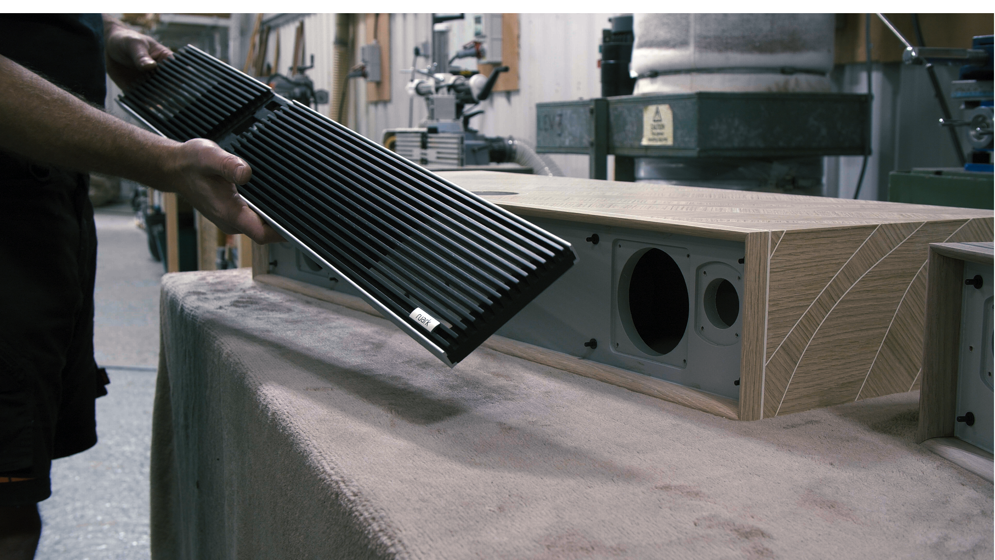 Ruark R810 MiE is hand assembled at Ruark's factory. A person holds a dark grid in front of an R810 MiE cabinet