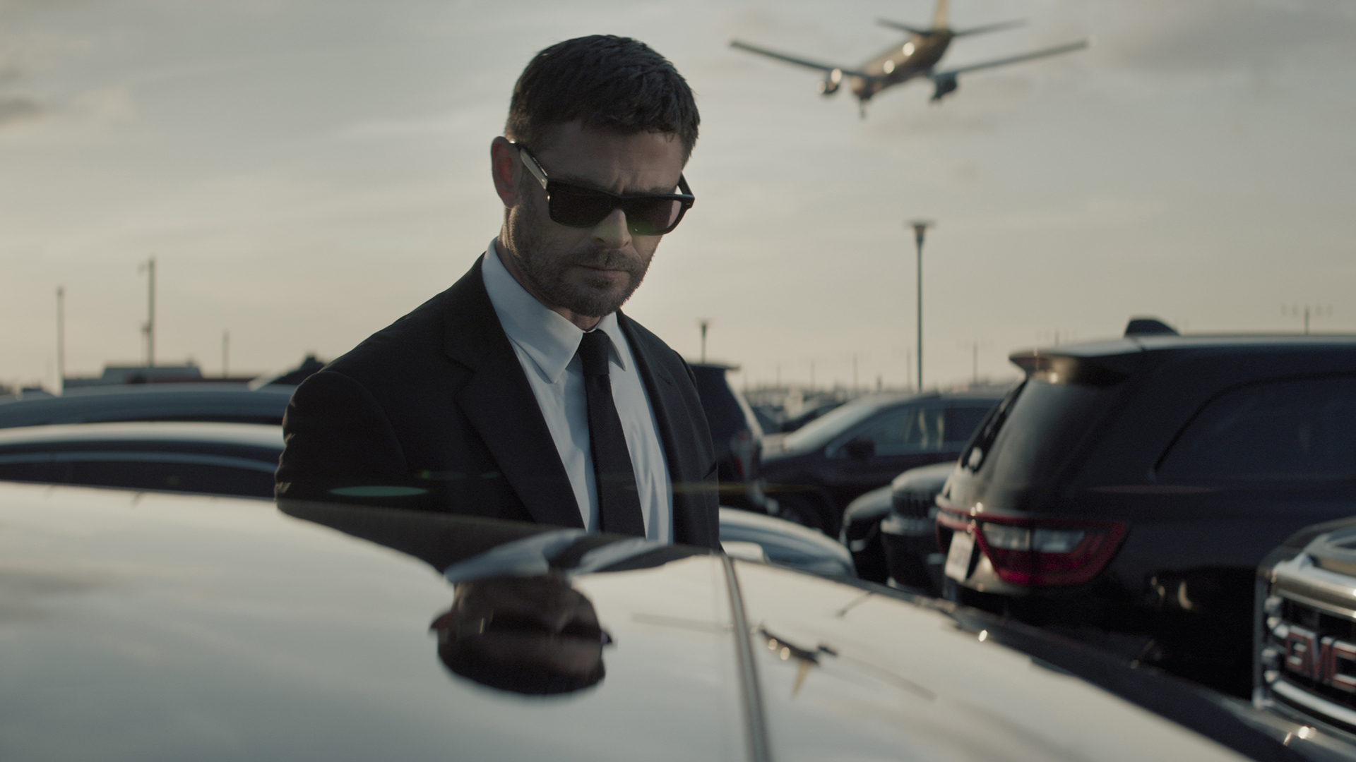 Mike Davis stands next to a car wearing sunglasses and a suit in Crime 101
