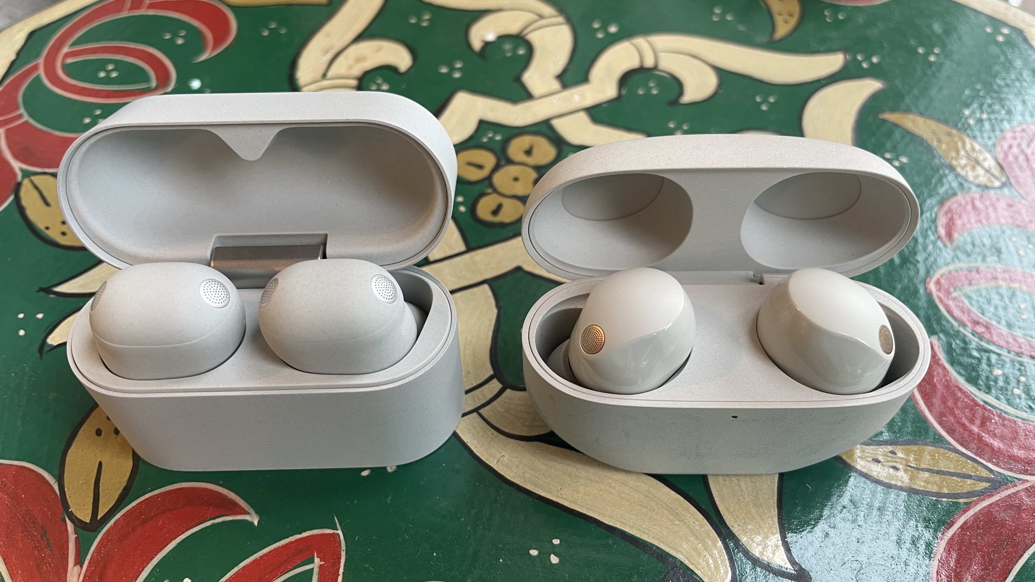 Sony WF-1000XM6 earphones next to the older generation. WF-1000XM5 and WF-C710N, on colorful table