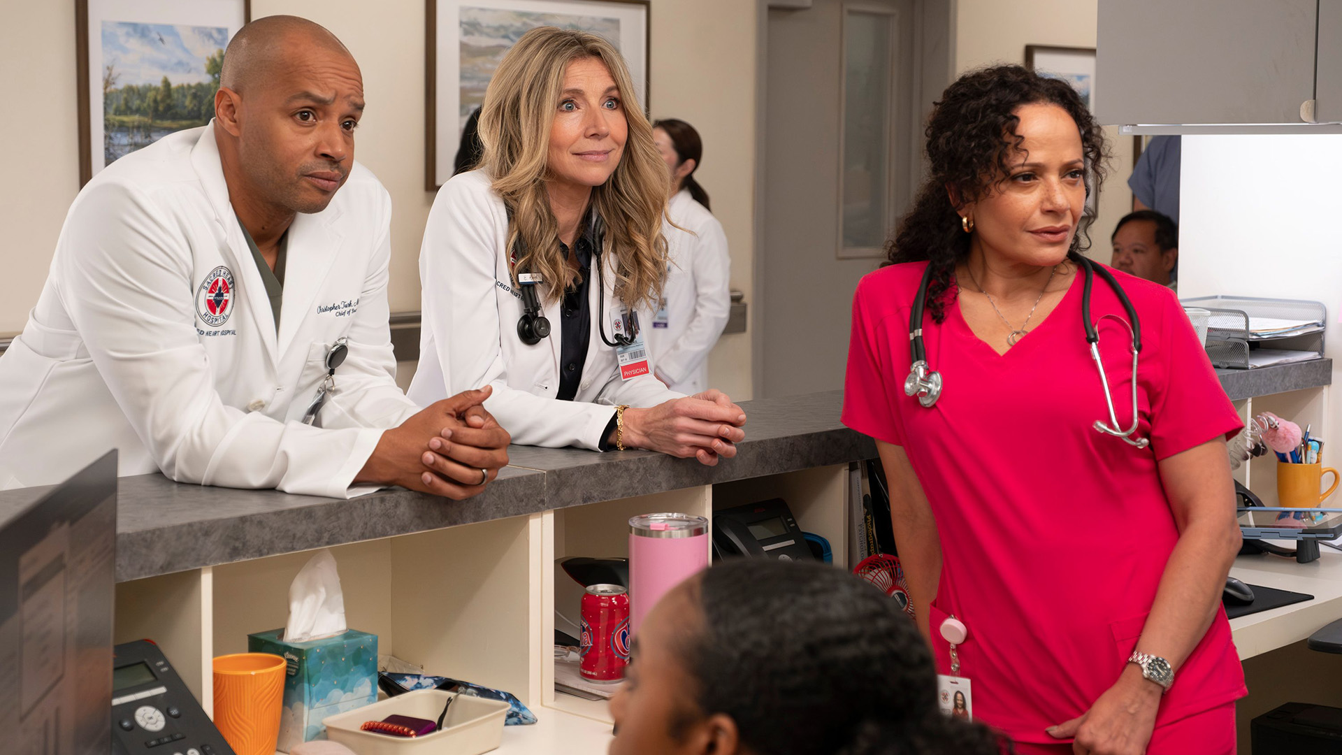 Turk and Elliot lean against a reception desk behind Carla in the Scrubs revival