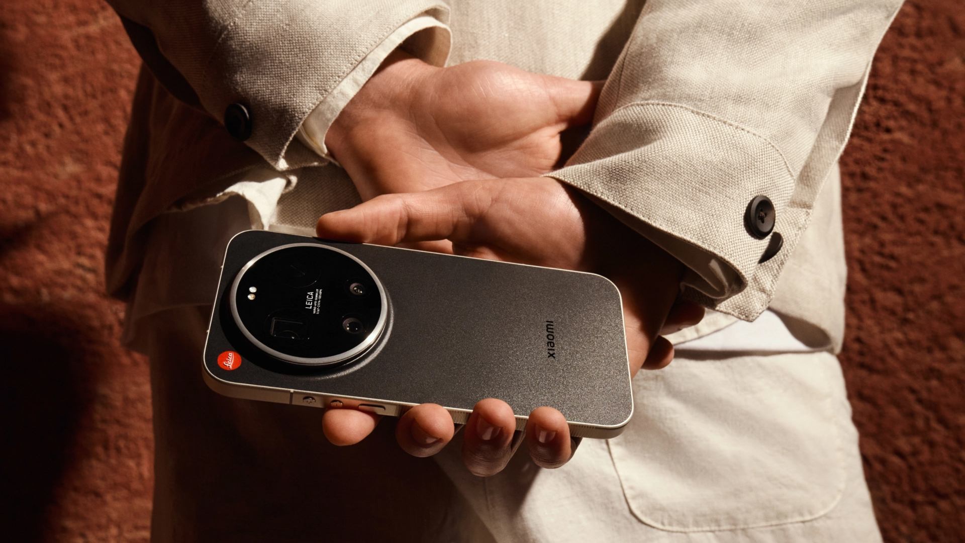 Leica Leitzphone in the user's hands, behind their back, with a dark red concrete wall background