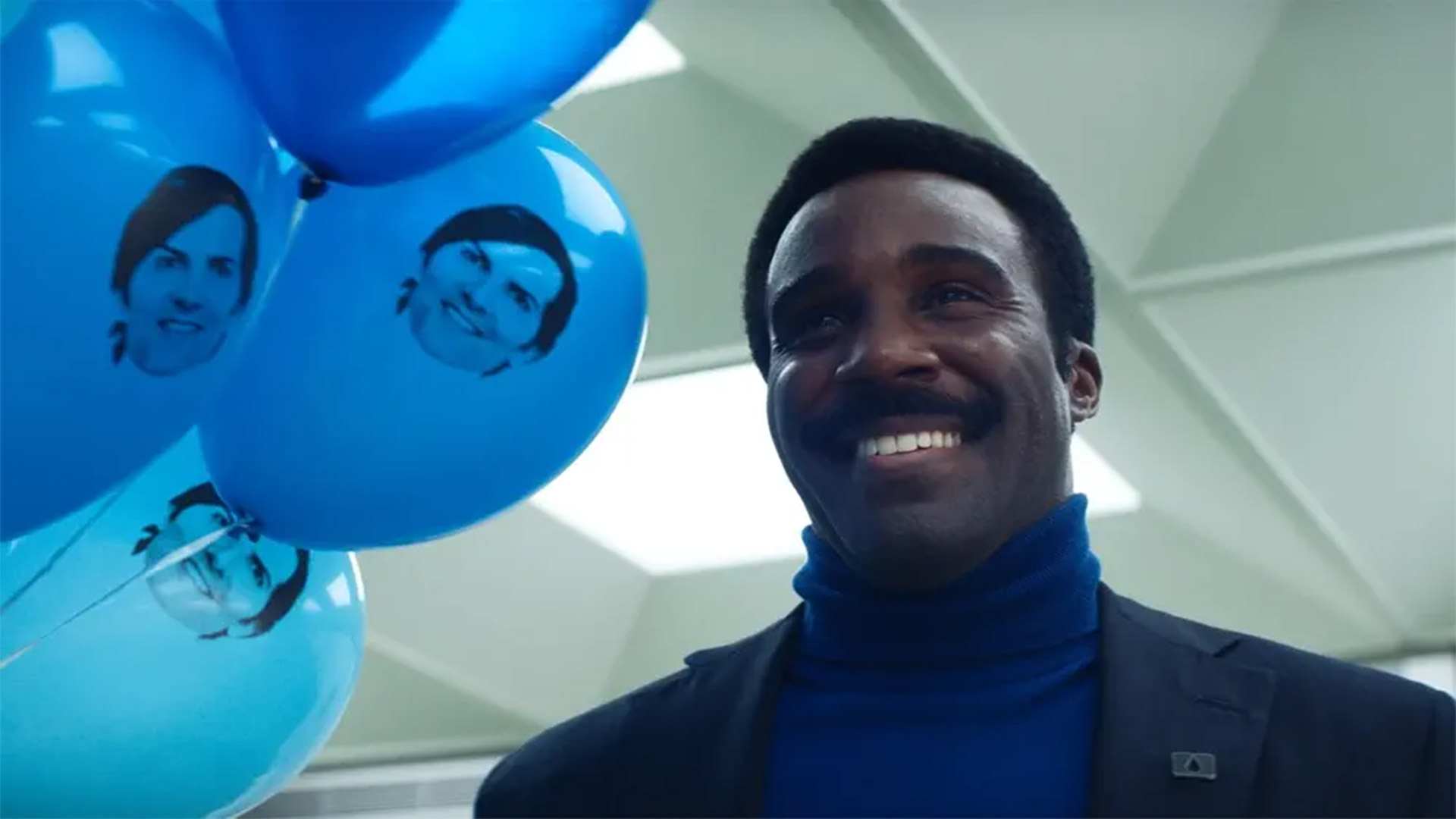 Tramell Tillman smiles next to balloons with Mark Scout's face on them