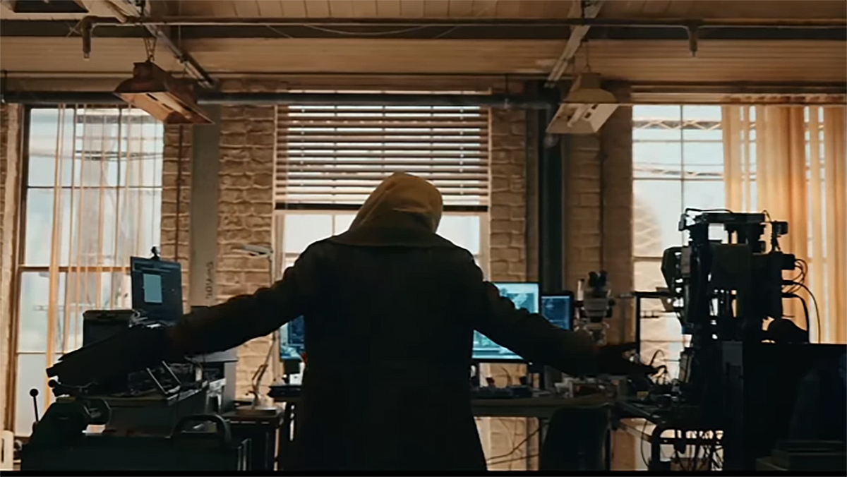 A hooded person slowly raising their hands while standing in front of a computer in Spider-Man: Brand New Day