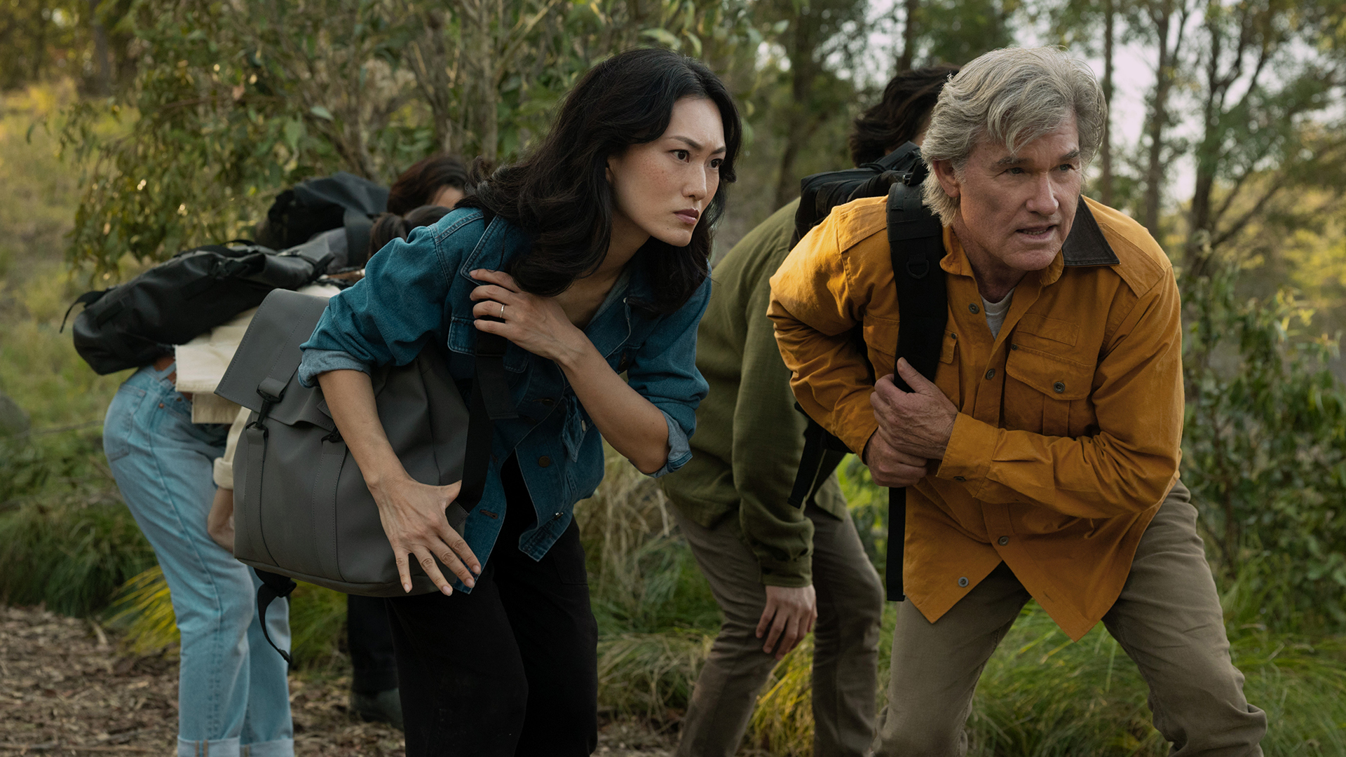 Keiko and Lee carry backpacks and crouch in a forest in Monarch: Legacy of Monsters Season 2 Episode 5
