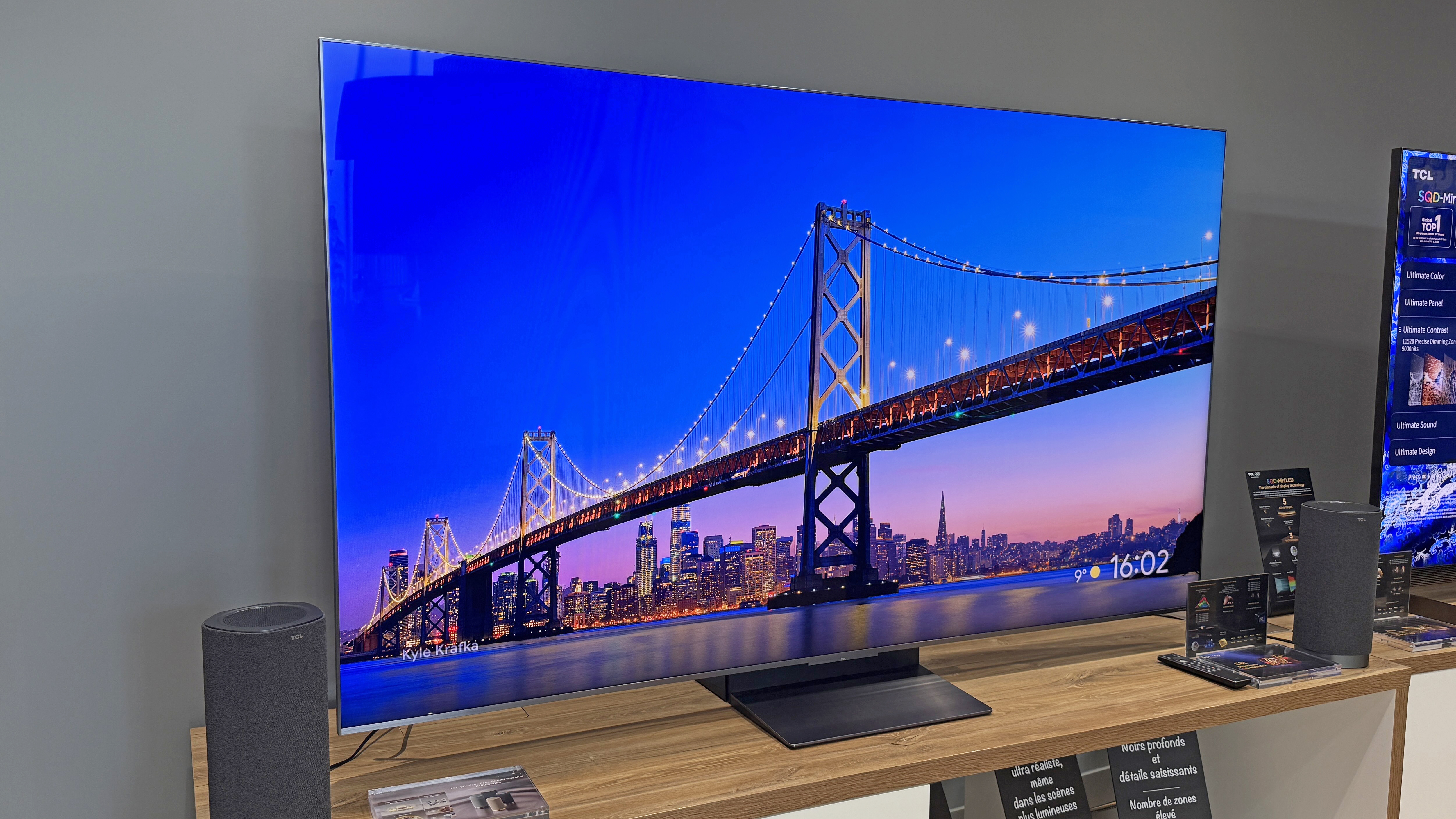 TCL C8L TV at a launch event showing a striking blue image of a large and the sky behind it