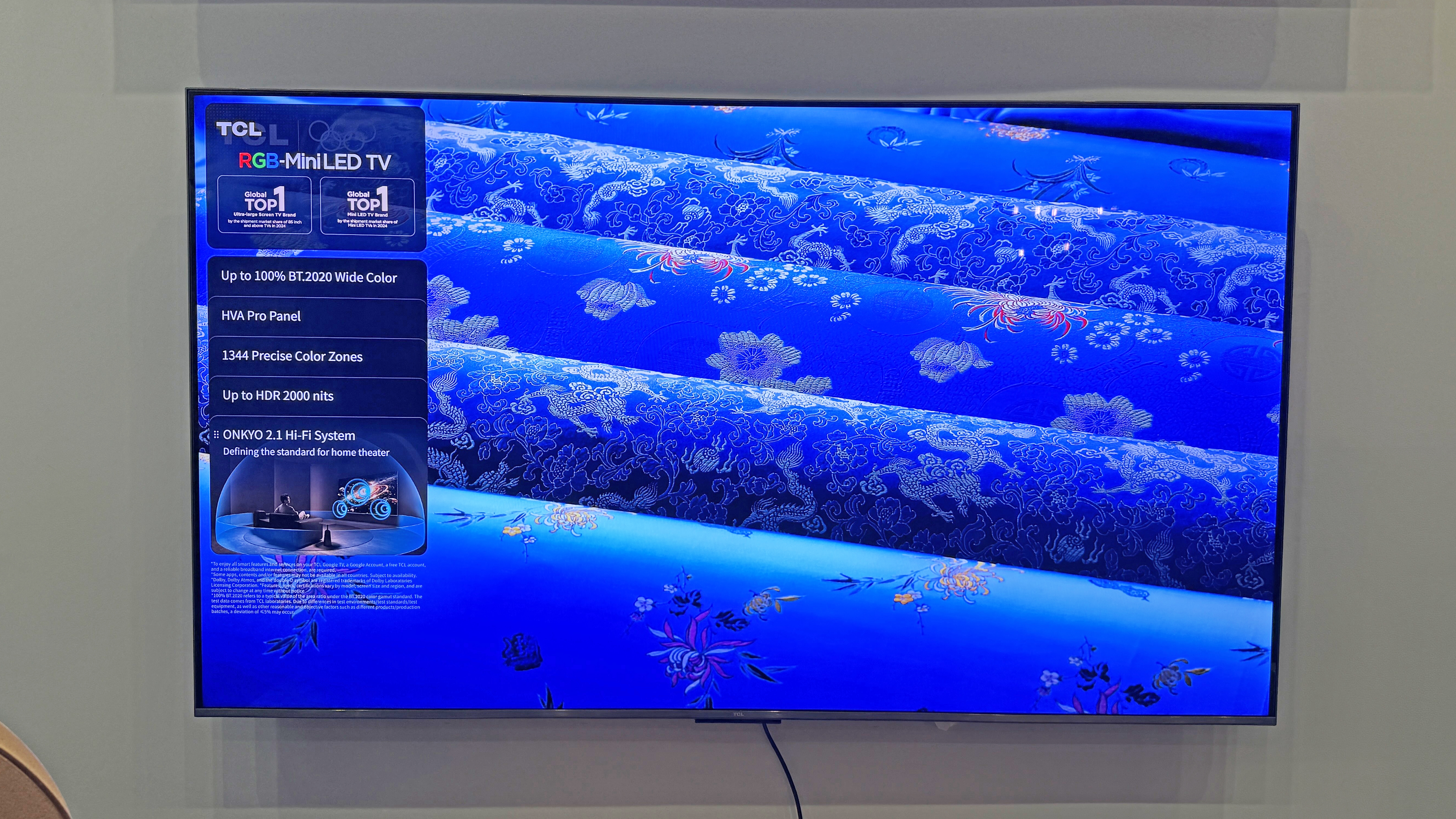 TCL RM7L TV at a launch event showing an image of rolls of blue fabric, with a bright and electric tone to the blue color