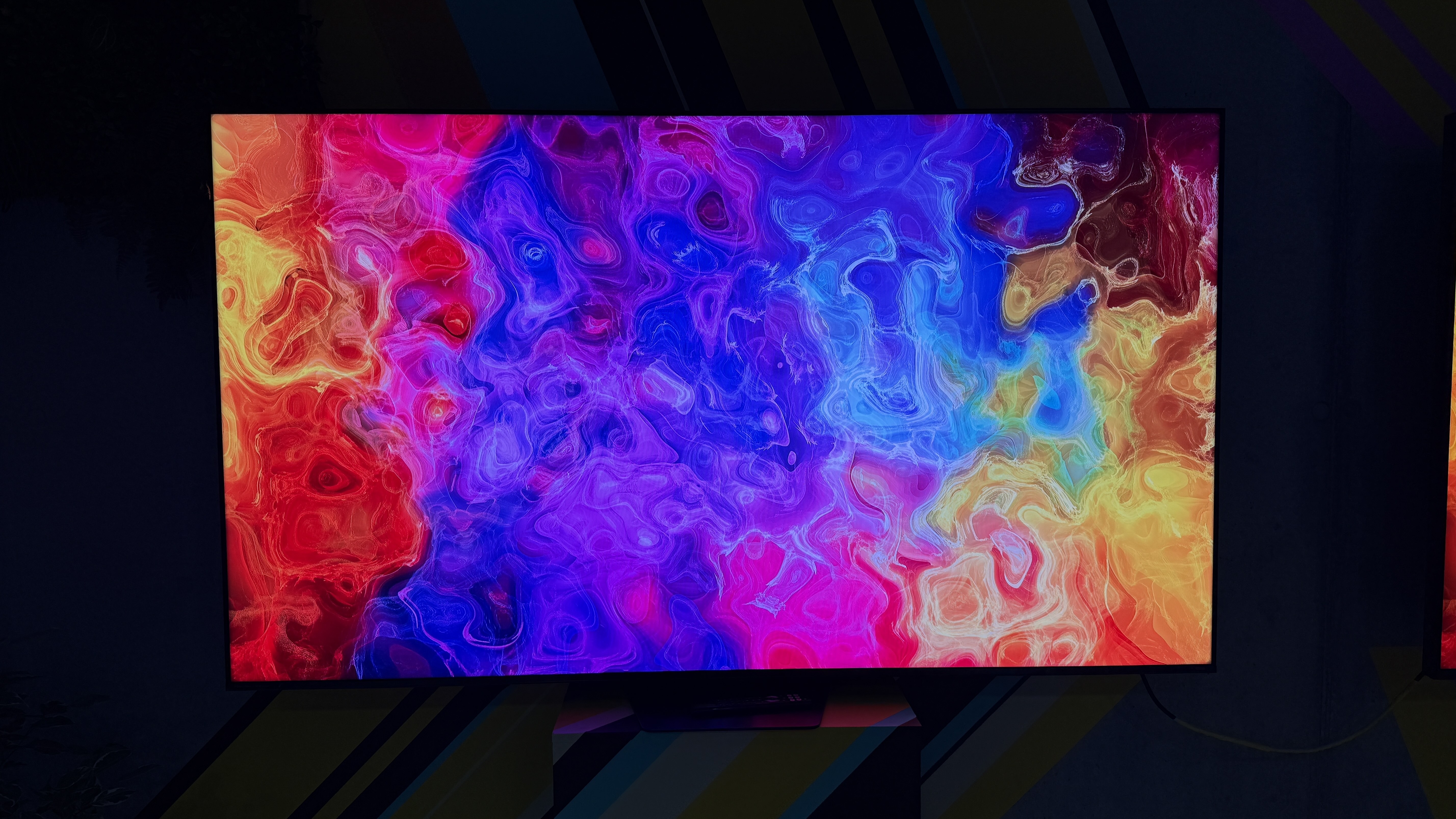 Hisense UR9S RGB TV in a dark room, with a pattern of rippling colors on the screen showing its impressive color reproduction