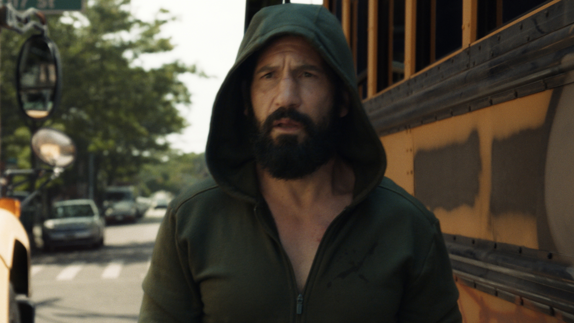 A hooded Frank Castle standing in front of an American school bus in The Punisher: One Last Kill