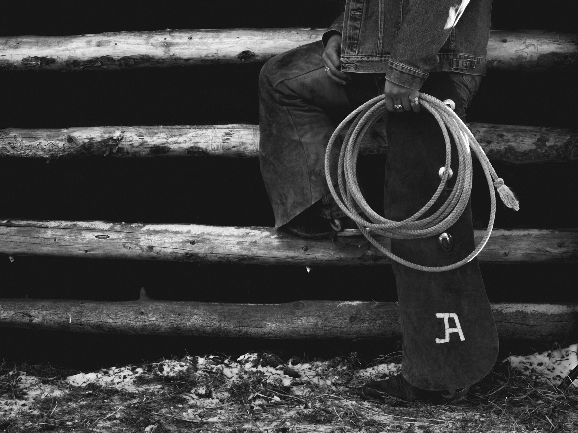 Black and white image of a cowboy model's legs, they are holding on to a rope