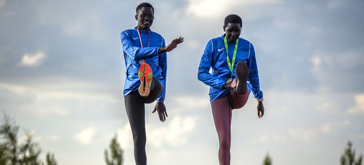 Two young African female athletes in blue tracksuits stretch on a running track at the Teryet National High Altitude Training Center in Uganda. The photo is part of a UNFPA documentation effort to highlight how athletics provides safe spaces and builds confidence for girls, especially survivors of female genital mutilation (FGM).