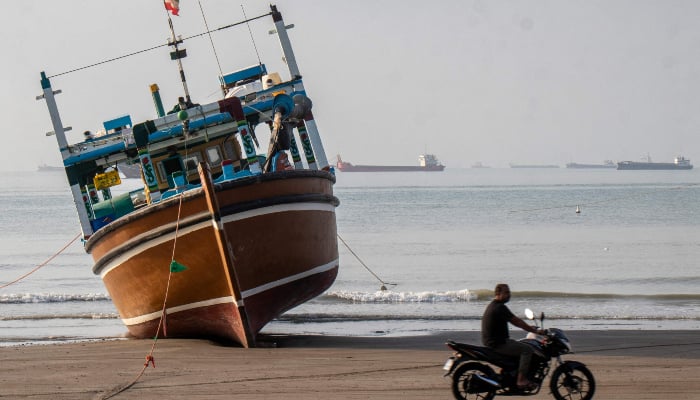 In this photo provided by Iran's ISNA news agency on April 24, 2026, an Iranian man rides his motorcycle past a boat at Suru Beach in Bandar Abbas along the Strait of Hormuz. — AFP
