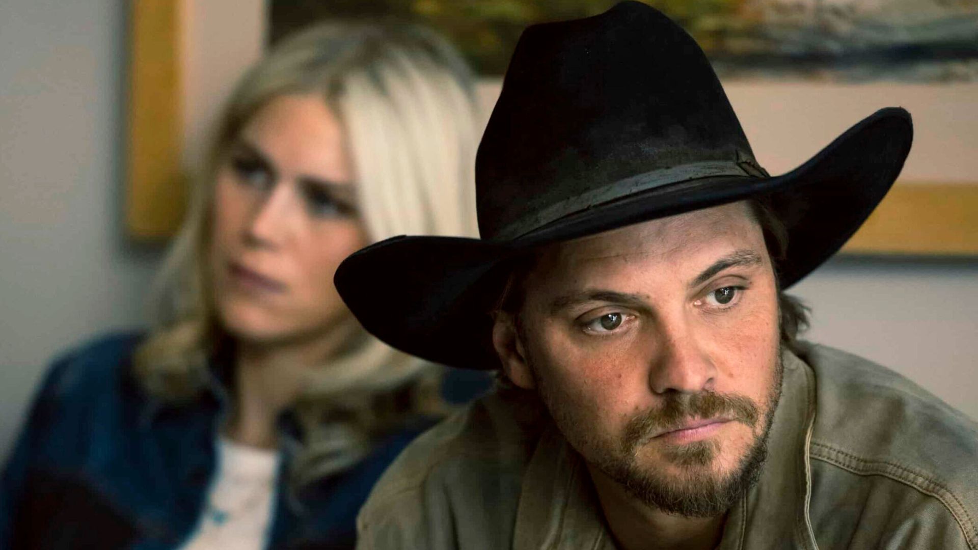 Kayce looks off into the distance as a blonde woman sits behind him