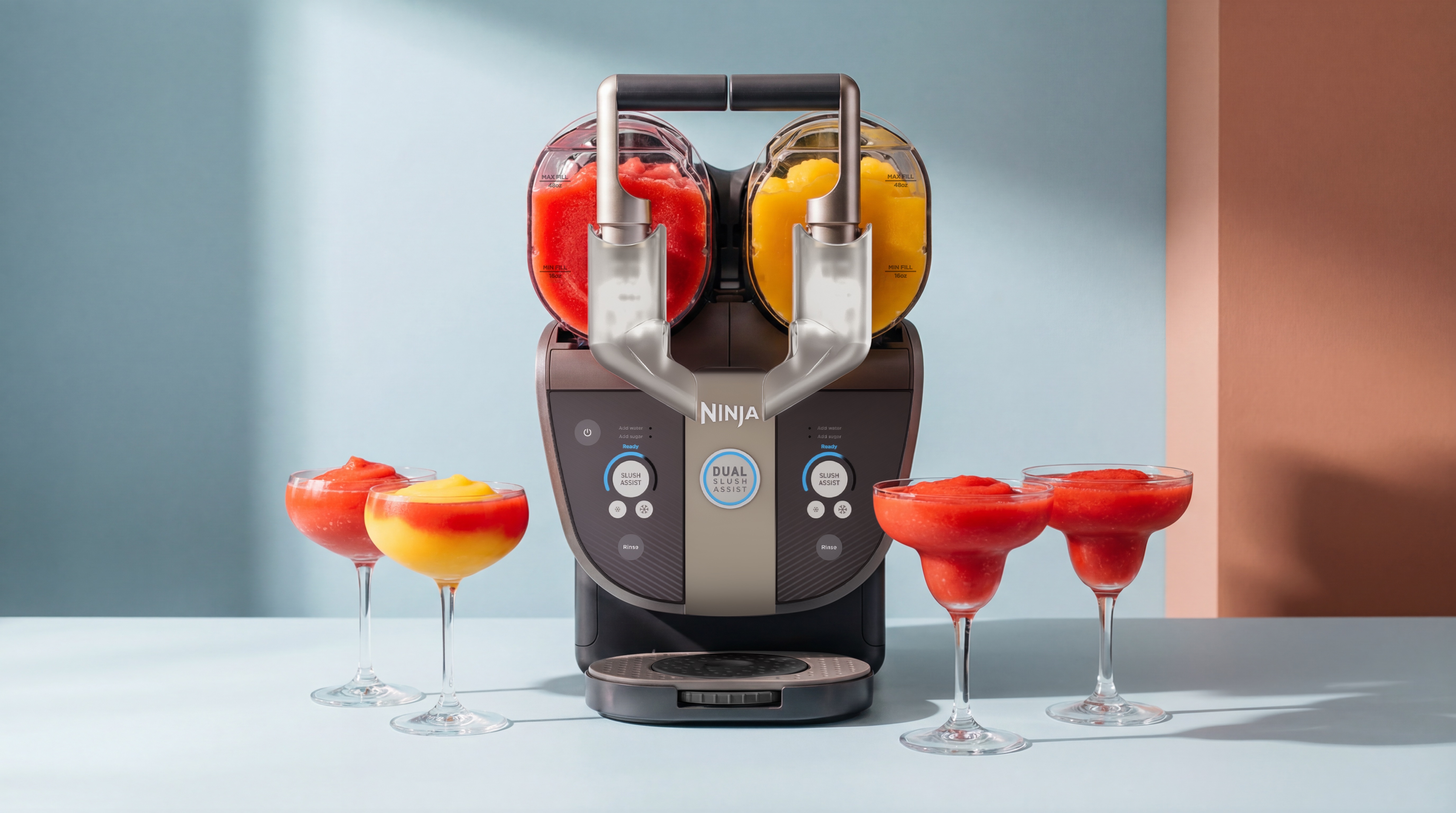 Ninja Slushi Twist on a light table top with a red drink in one chamber and a yellow one in the other. There are four brightly colored drinks in cocktail glasses in front.