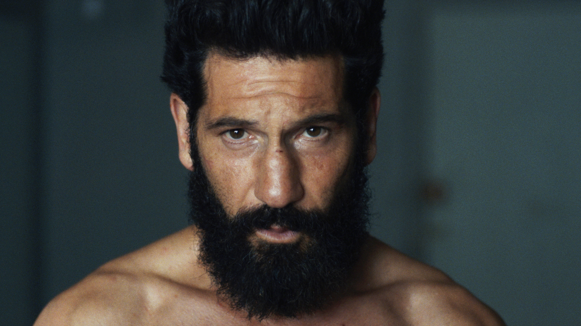 Head and shoulders shot of Jon Bernthal's bearded Frank Castle shirtless looking into the camera in The Punisher: One Last Kill