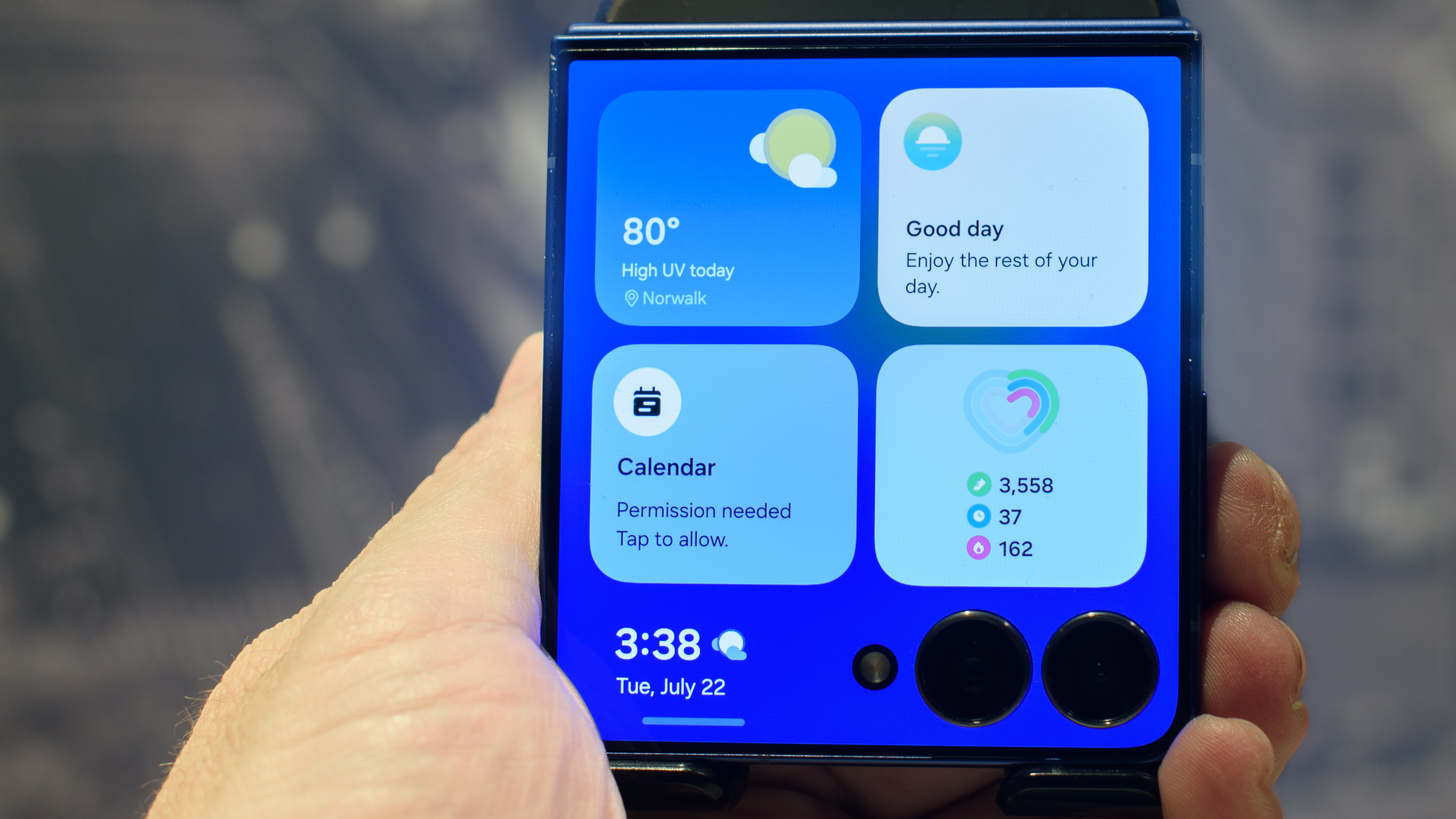 Samsung Galaxy Z Flip 7 in blue in hand shows four widgets on the cover screen including weather, now map, calendar and health monitor