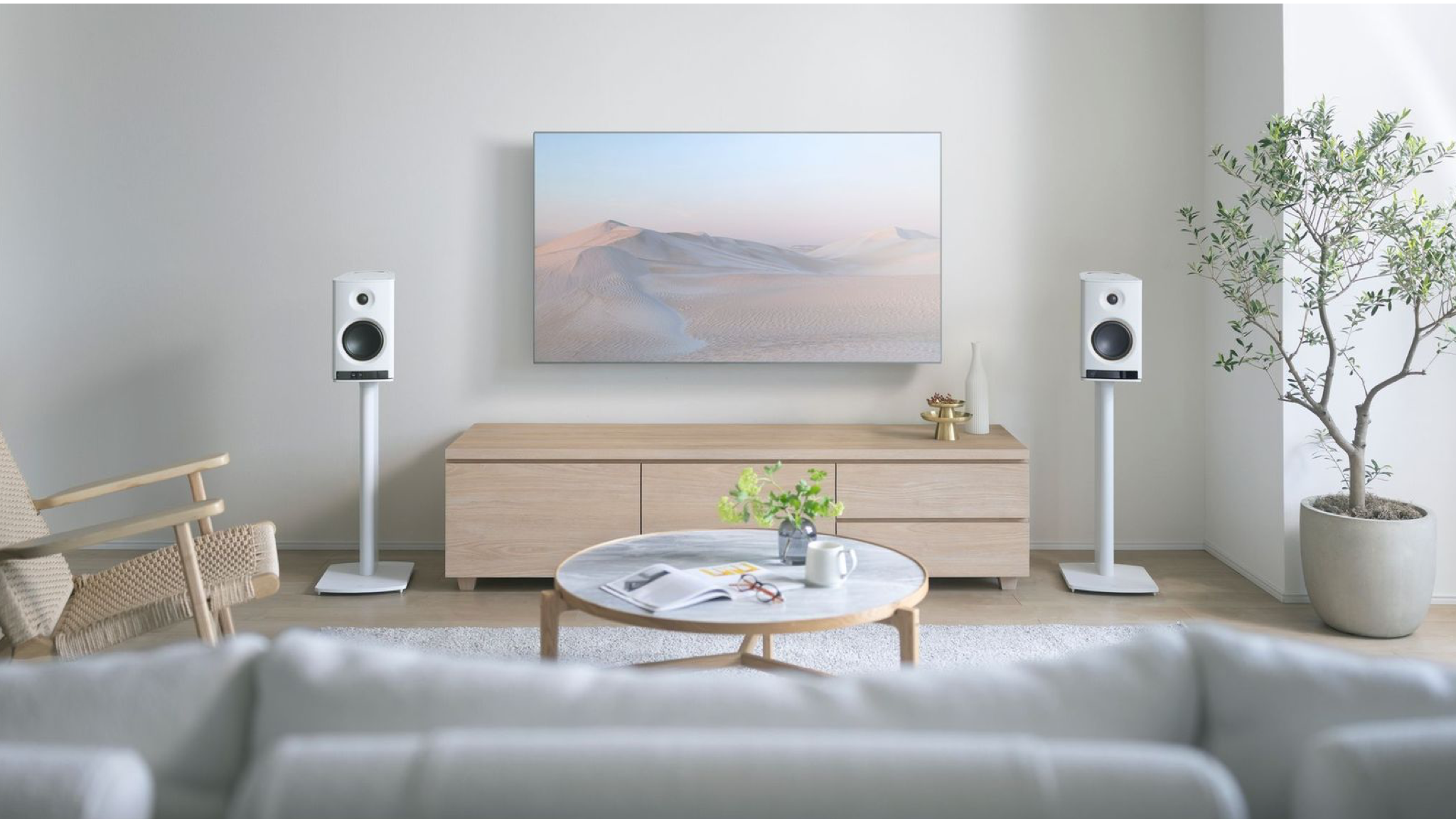 Yamaha NX-70A speakers in white in a neutrally decorated, brightly lit room. They stand on stands on either side of a wall-mounted television.