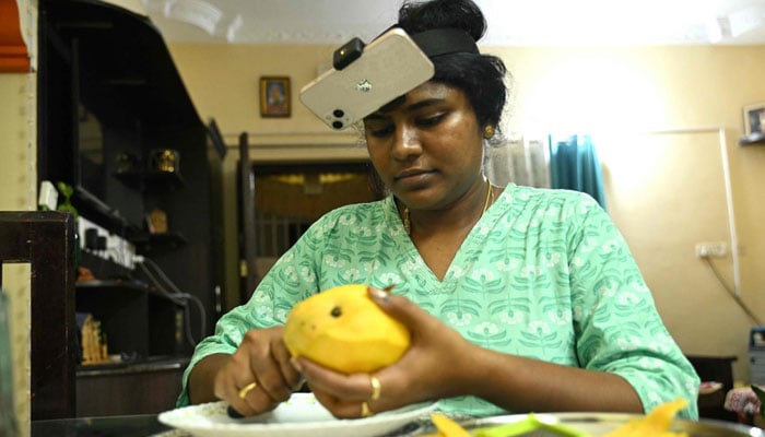 An Indian housewife Nagireddy Sriramyachandra wearing a smartphone on her head as she records her actions through motion capture while cutting mangoes at her home in Chennai. — AFP